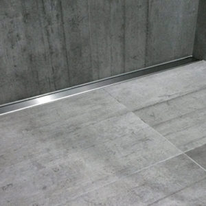 Stainless steel shower channel floor drain against wall with grey bathroom tiles walk in tiled shower strip drain alcove